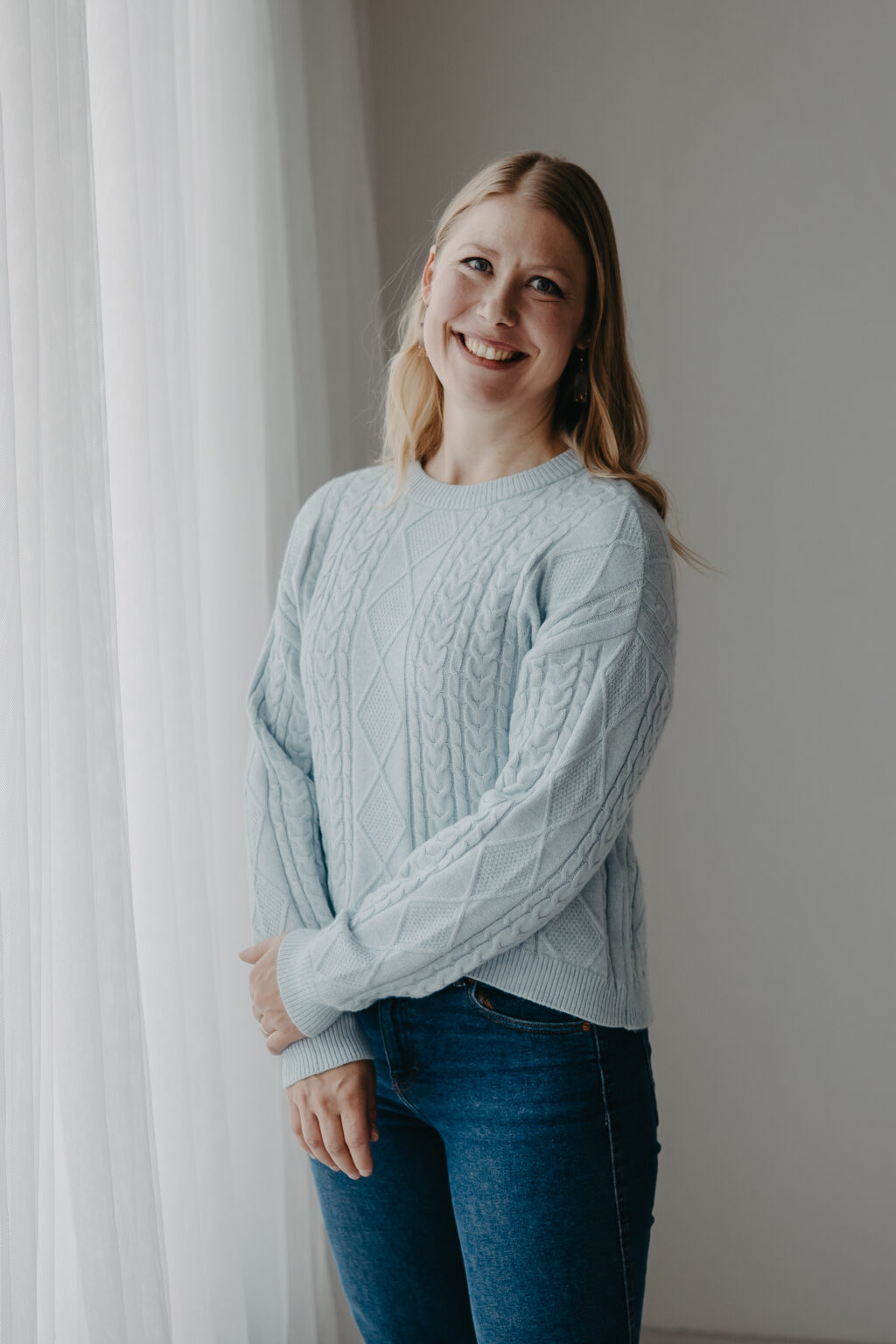 Miina Tauriala, puheterapeutti, hymyilee kameralle vaaleassa neuleessa.