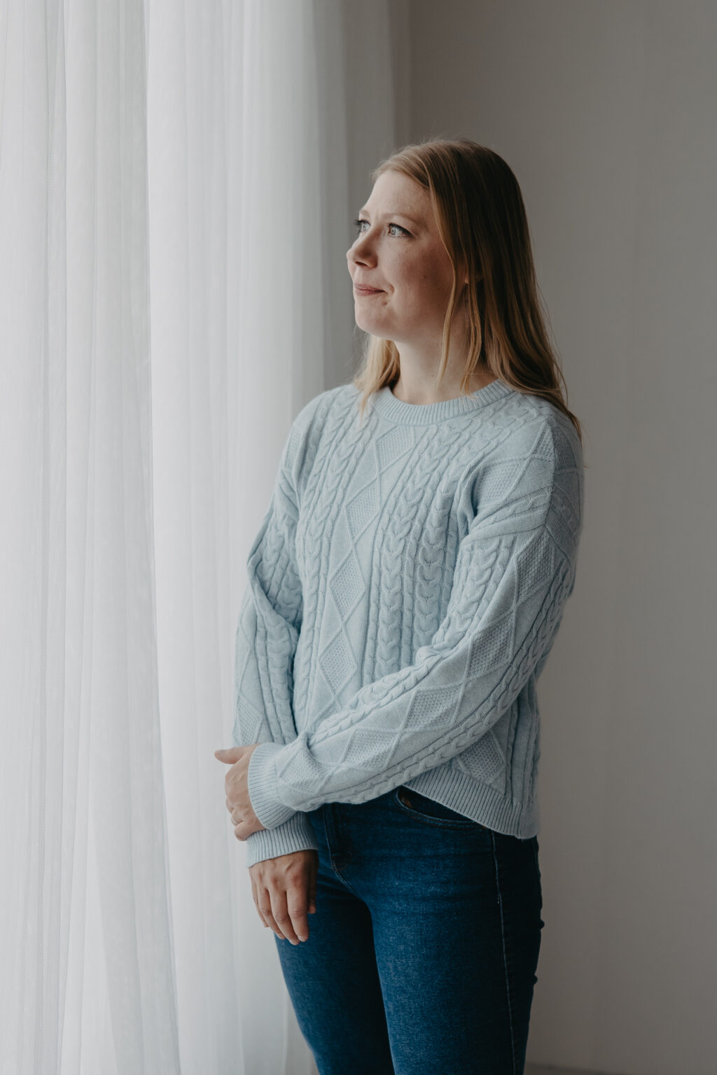 Miina Tauriala, puheterapeutti, katsoo ikkunasta vaaleassa neuleessa.