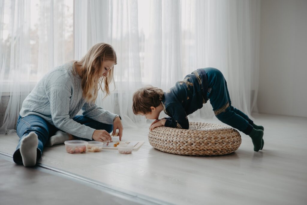 Puheterapeutti ja lapsi harjoittelevat vuorovaikutusta ja hienomotoriikkaa leikin avulla lattialla.