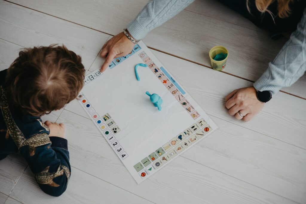 Puheterapeutti ja lapsi harjoittelevat kuvakommunikointia kuvataulun ja muovailuvahasta tehtyjen hahmojen avulla.